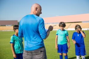 a male coach guiding his team on the sports field during a practice session.